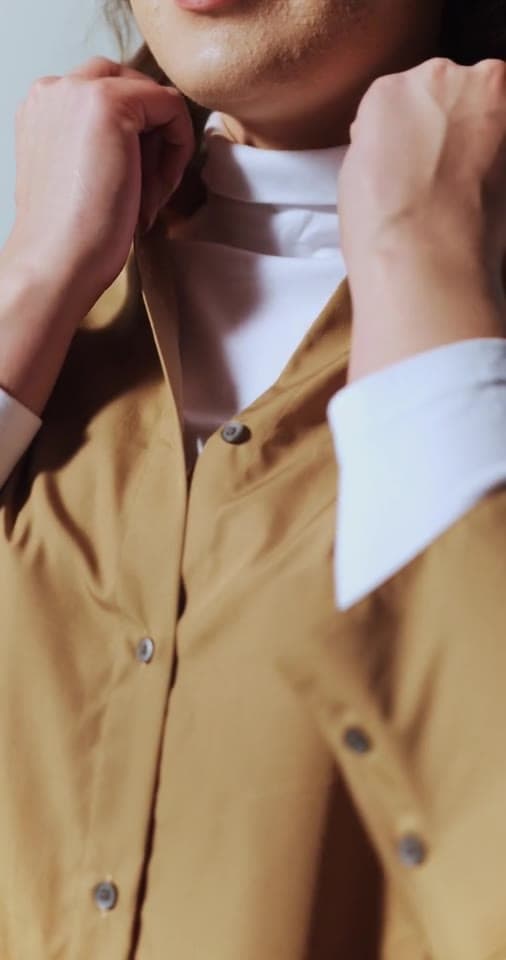 Example video: hands buttoning the collar of a camel button-up shirt